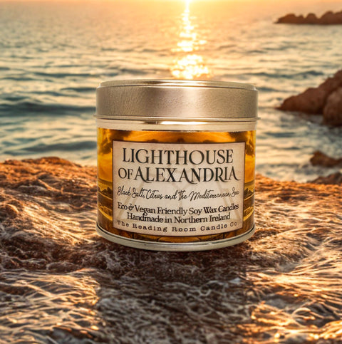 Candle labeled 'Lighthouse of Alexandria' on a rocky beach with sunset in the background