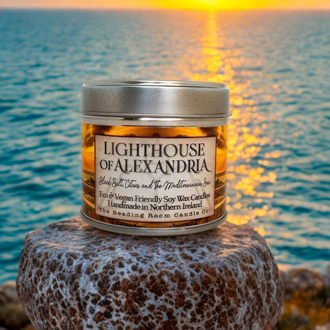 Candle jar labeled 'Lighthouse of Alexandria' on a rock with sunset over water in the background
