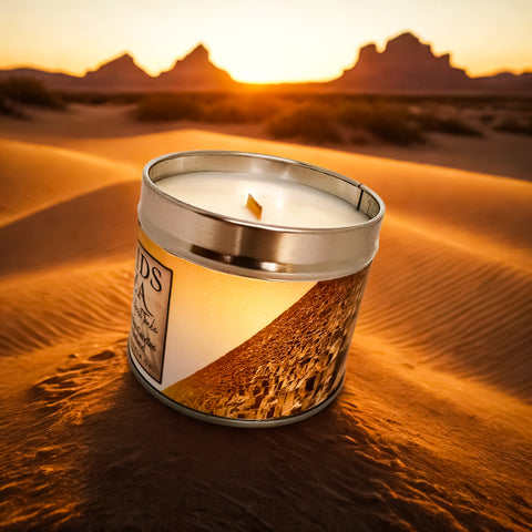 Candle in a metal container on sand dunes with sunset in the background