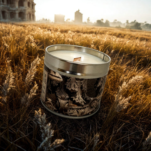 Candle in a decorative tin with intricate designs, placed in a field with ruins in the background