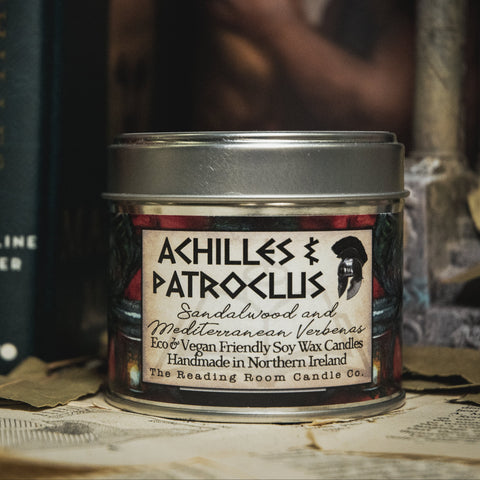 Soy Wax Candle labeled 'Achilles & Patroclus' on a surface with books and leaves in the background