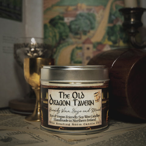 Soy Wax Candle tin labeled 'The Old Dragon Tavern' on a surface with a blurred bookish background