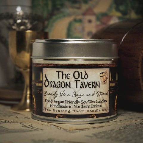 Soy Wax Candle tin labeled 'The Old Dragon Tavern' on a surface with a blurred bookish background