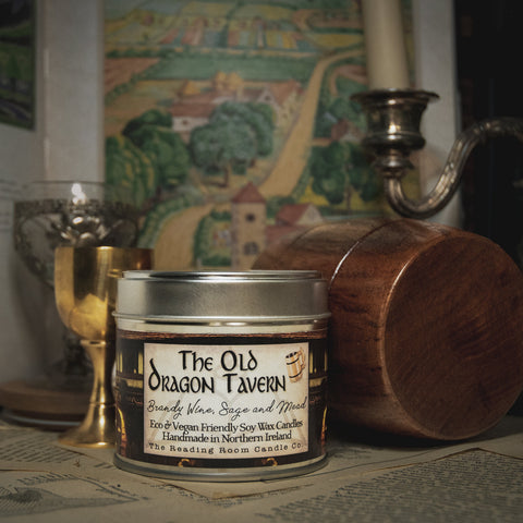 Soy Wax Candle tin labeled 'The Old Dragon Tavern' on a surface with a blurred bookish background
