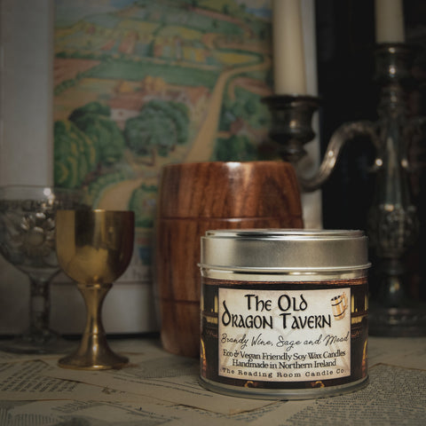 Soy Wax Candle tin labeled 'The Old Dragon Tavern' on a surface with a blurred bookish background