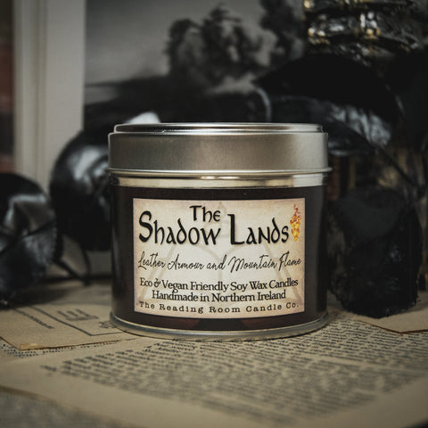 Soy Wax Candle tin labeled 'The Shadow Lands' on an open book with a dark, moody background.
