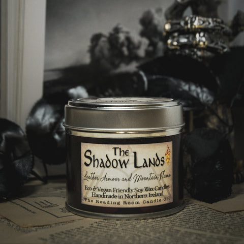 Soy Wax Candle tin labeled 'The Shadow Lands' on an open book with a dark, moody background.