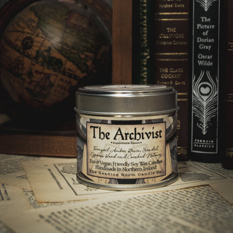 Soy Wax Candle labeled 'The Archivist' on a surface with books in the background