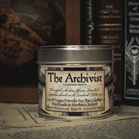 Soy Wax Candle labeled 'The Archivist' on a surface with books in the background