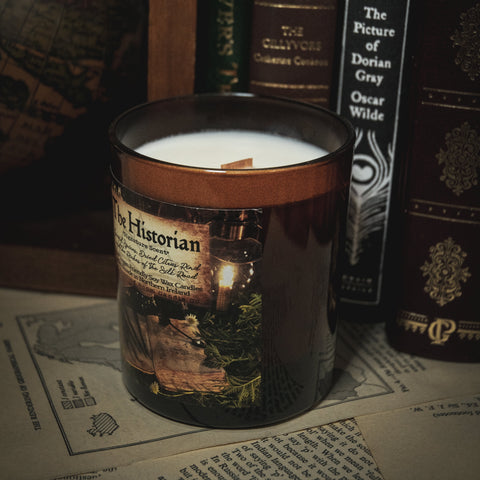 Soy Wax Candle tin labeled 'The Historian' on a surface with books in the background