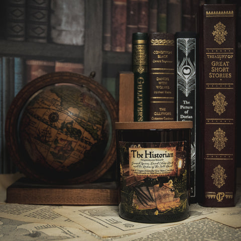 Soy Wax Candle tin labeled 'The Historian' on a surface with books in the background