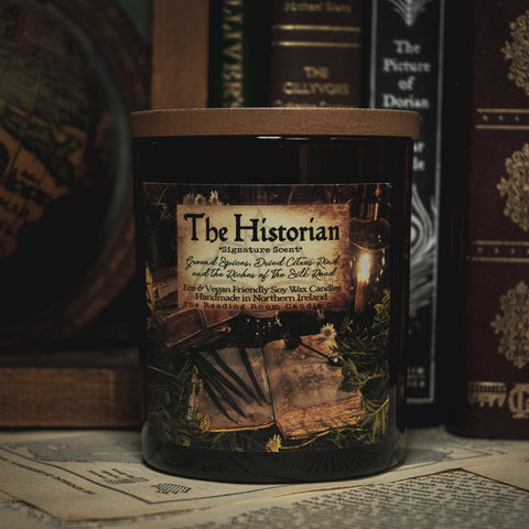 Soy Wax Candle tin labeled 'The Historian' on a surface with books in the background