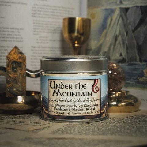 Candle jar labeled 'Under the Mountain' on a surface with books and decorative items in the background