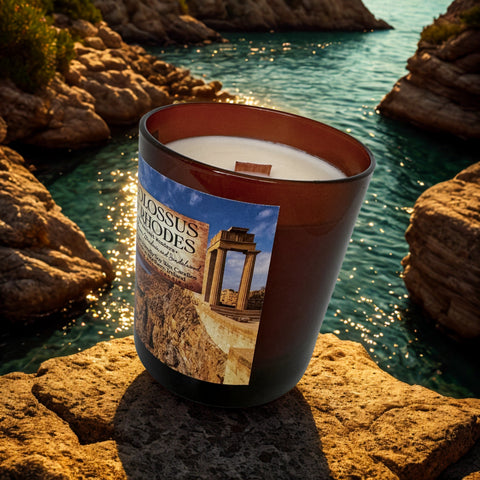 Candle with a 'Colossus of Rhodes' label on a rocky shore with water in the background