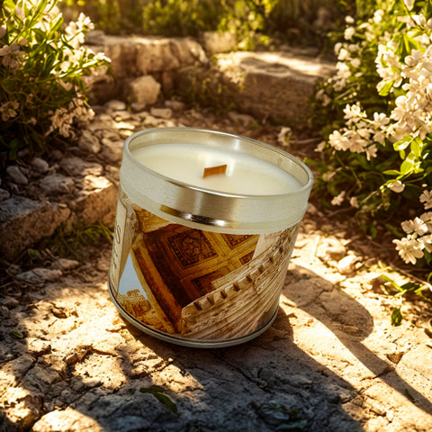 Candle in a decorative tin with a rustic design on a stone surface surrounded by flowers